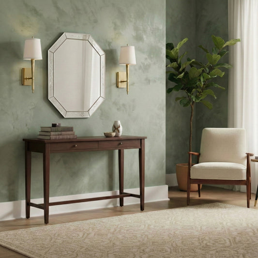 Decorative console table with a murano glass mirror and a pair of brass sconces against a green limewash wall in a living room setting.