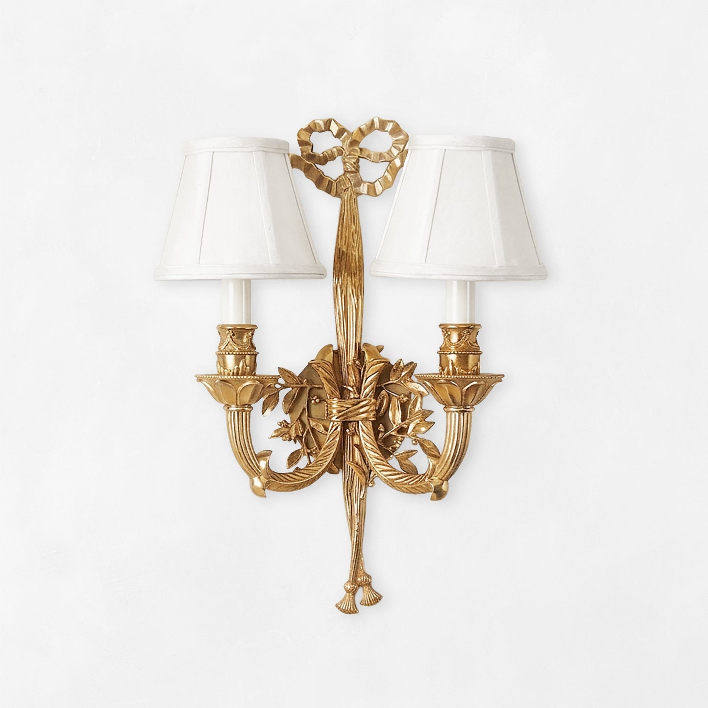 Ornate antique brass sconce with ribbon motif and white shades.