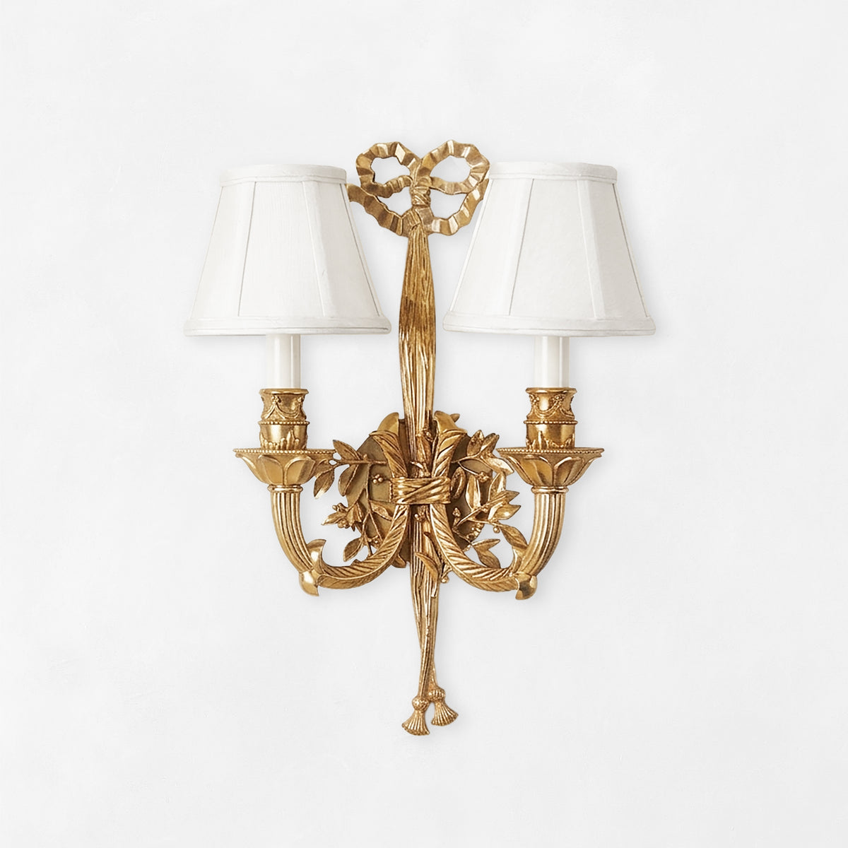 Luxurious brass sconce with ribbon motif and white shades.