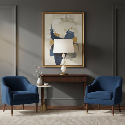 Two blue armchairs in a living room with a abstract painting and an alabaster lamp on a console table.