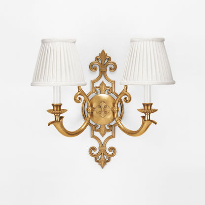 An antique brass sconce with pleated white shades.
