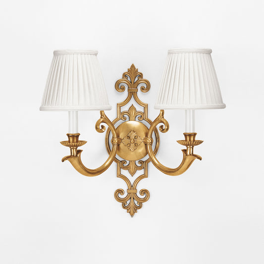 An antique brass sconce with pleated white shades.