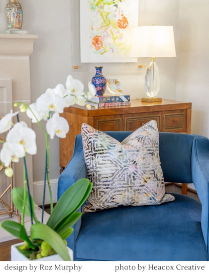 Blue velvet armchair with a patterned pillow, white orchids, and a high end crystal and antique brass table lamp in a luxurious living room.