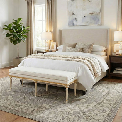 Neatly made bed with white bedding, alabaster lamps and a gold-leaf bench in a bedroom setting.