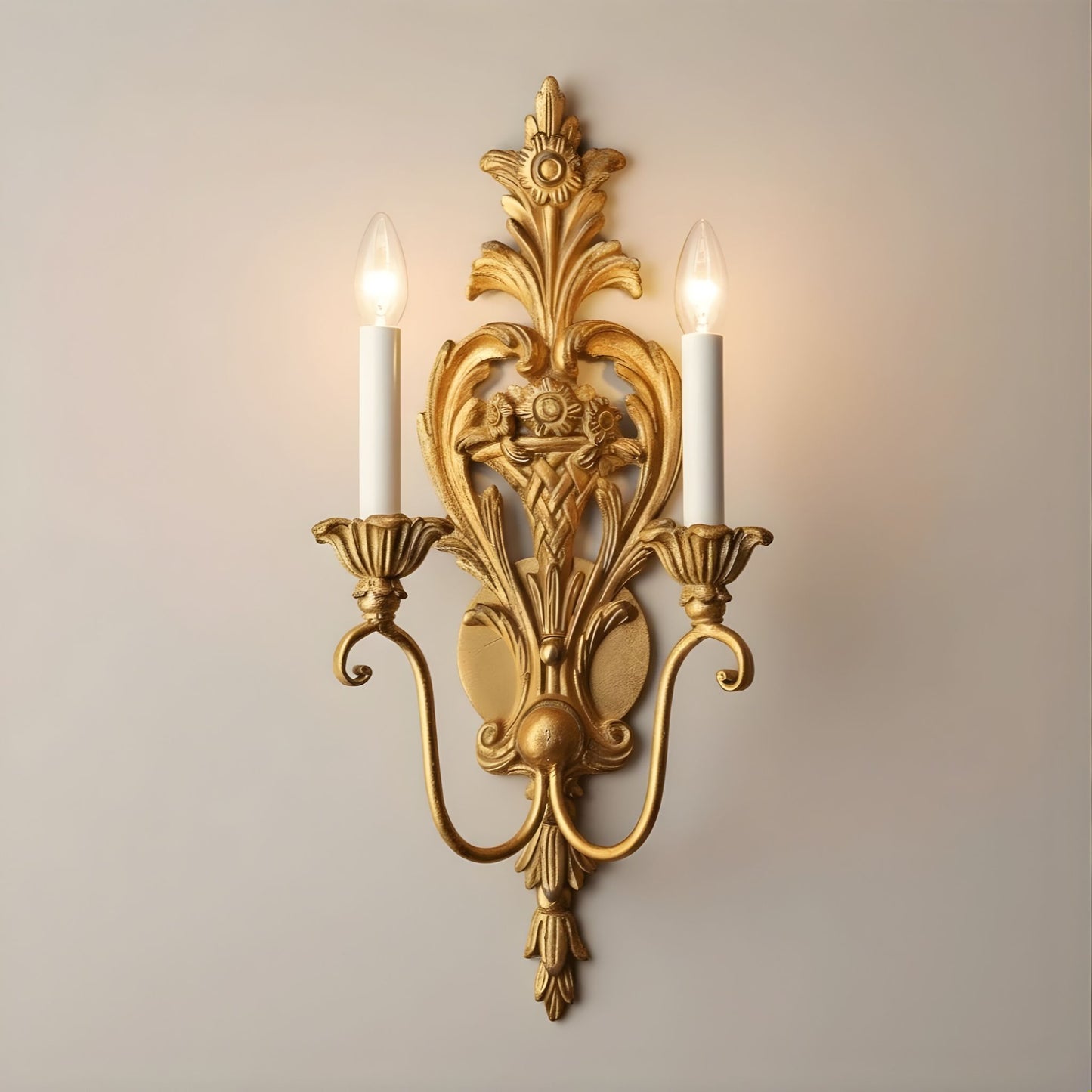 Decorative gold leaf wall sconce with two lit candles on a plain background