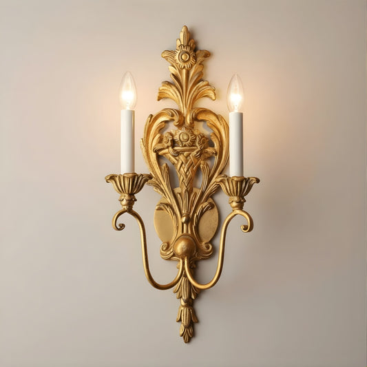 Decorative gold leaf wall sconce with two lit candles on a plain background