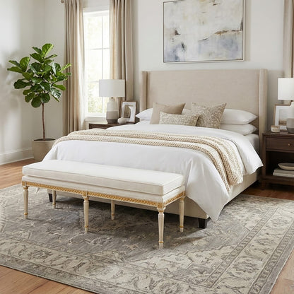 Neatly made bed with white bedding and decorative pillows with a handmade gold-leaf Italian bench.
