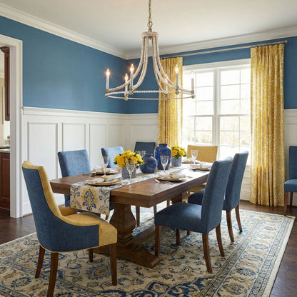 Dining room with wooden table and blue chairs, featuring a handmade silver chandelier and large windows.
