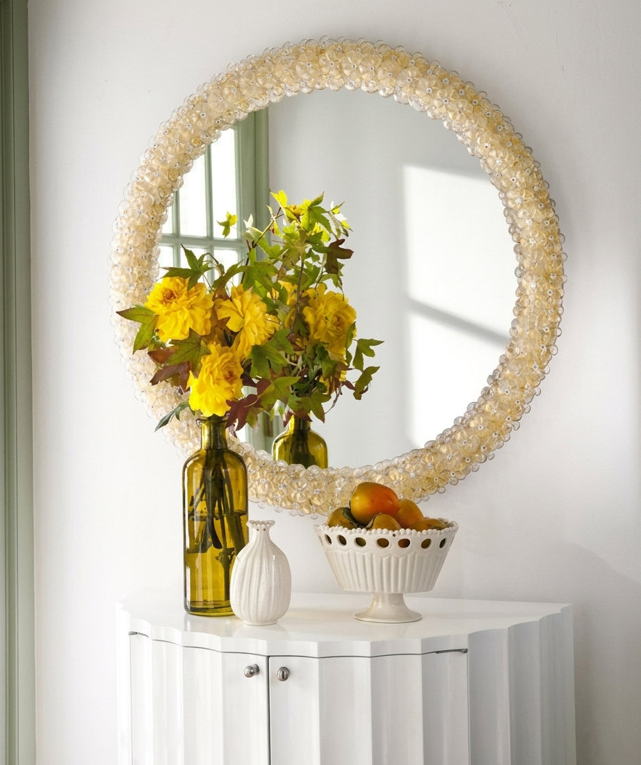Round gold Venetian glass mirror next to flowers and decor.