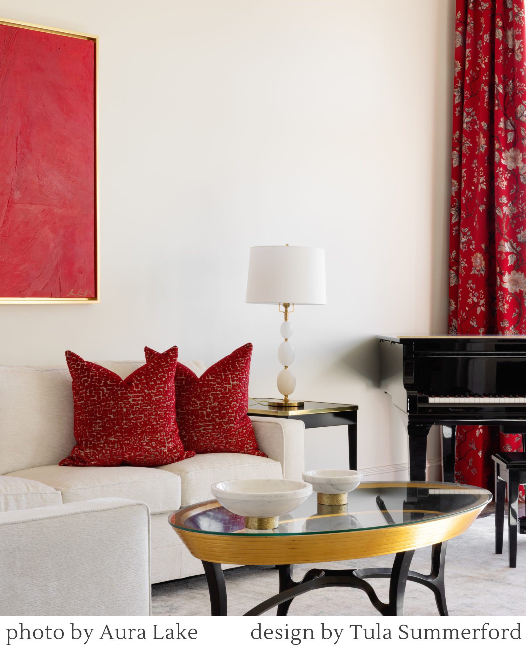 Luxurious living room with red pillows on a white sofa, gold coffee table, piano, and alabaster lamp.