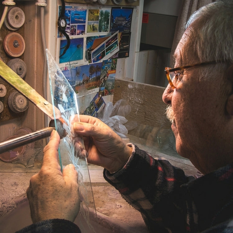 An Italian artisan engraves a Murano glass mirror component.