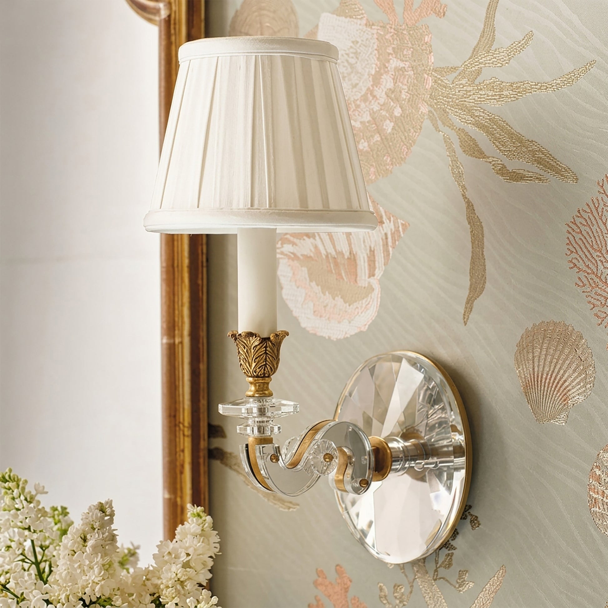 Antique brass sconce with crystal details and a white pleated shade next to a traditional mirror.