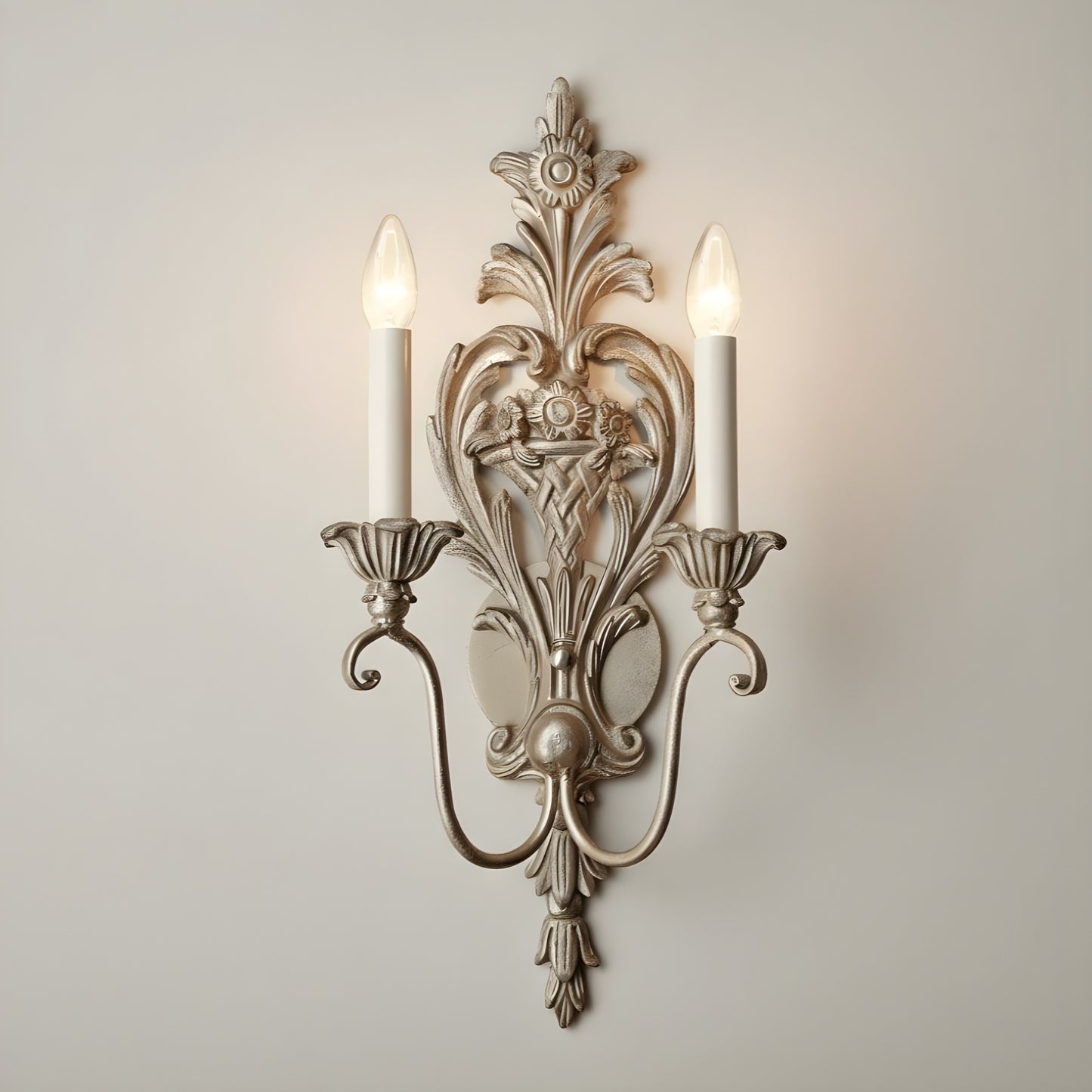 Decorative silver-leaf wall sconce with two lit candles on a plain wall.