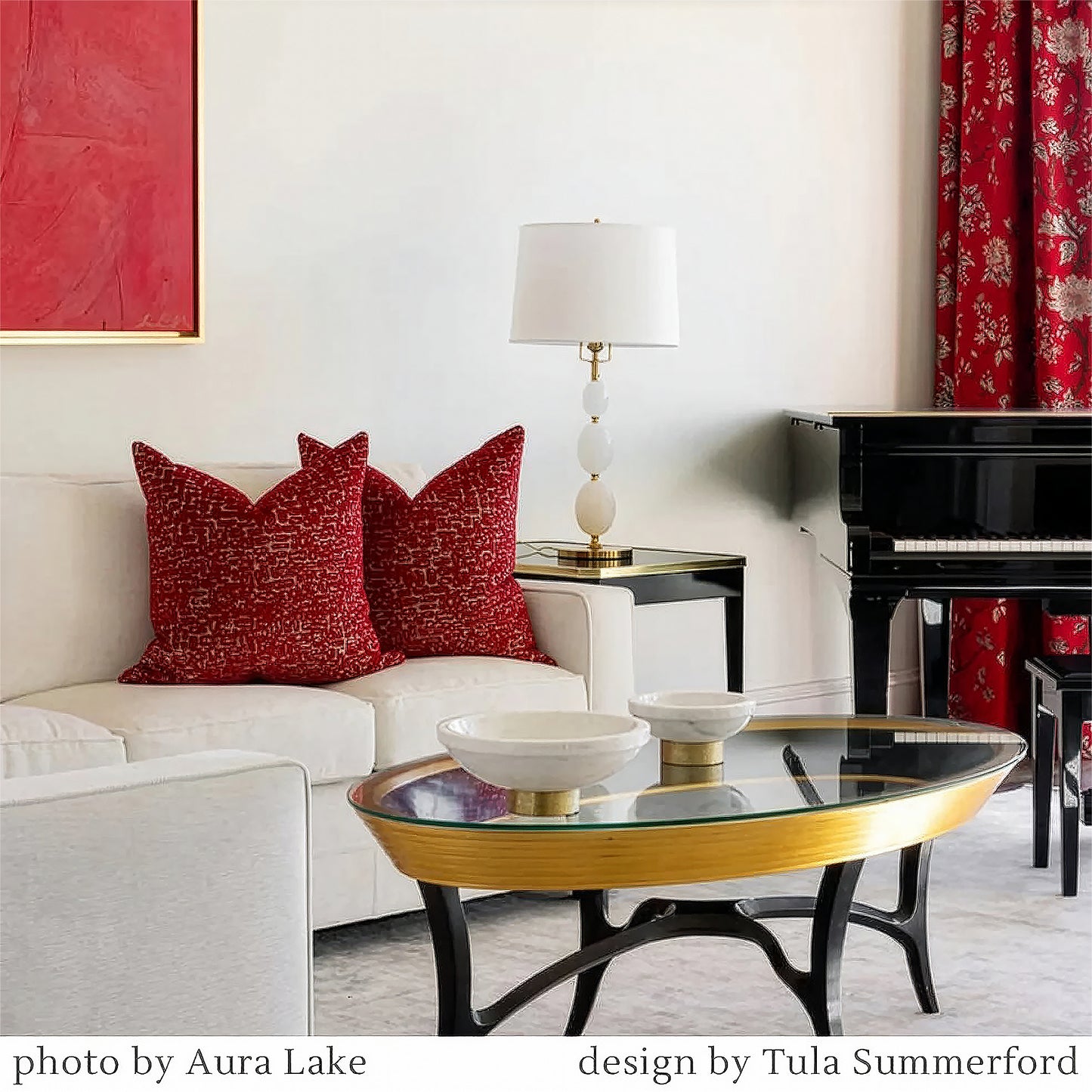 Living room with red pillows on a white sofa, glass coffee table, piano, and brass lamp.