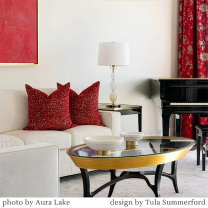 Living room with red pillows on a white sofa, glass coffee table, piano, and brass lamp.
