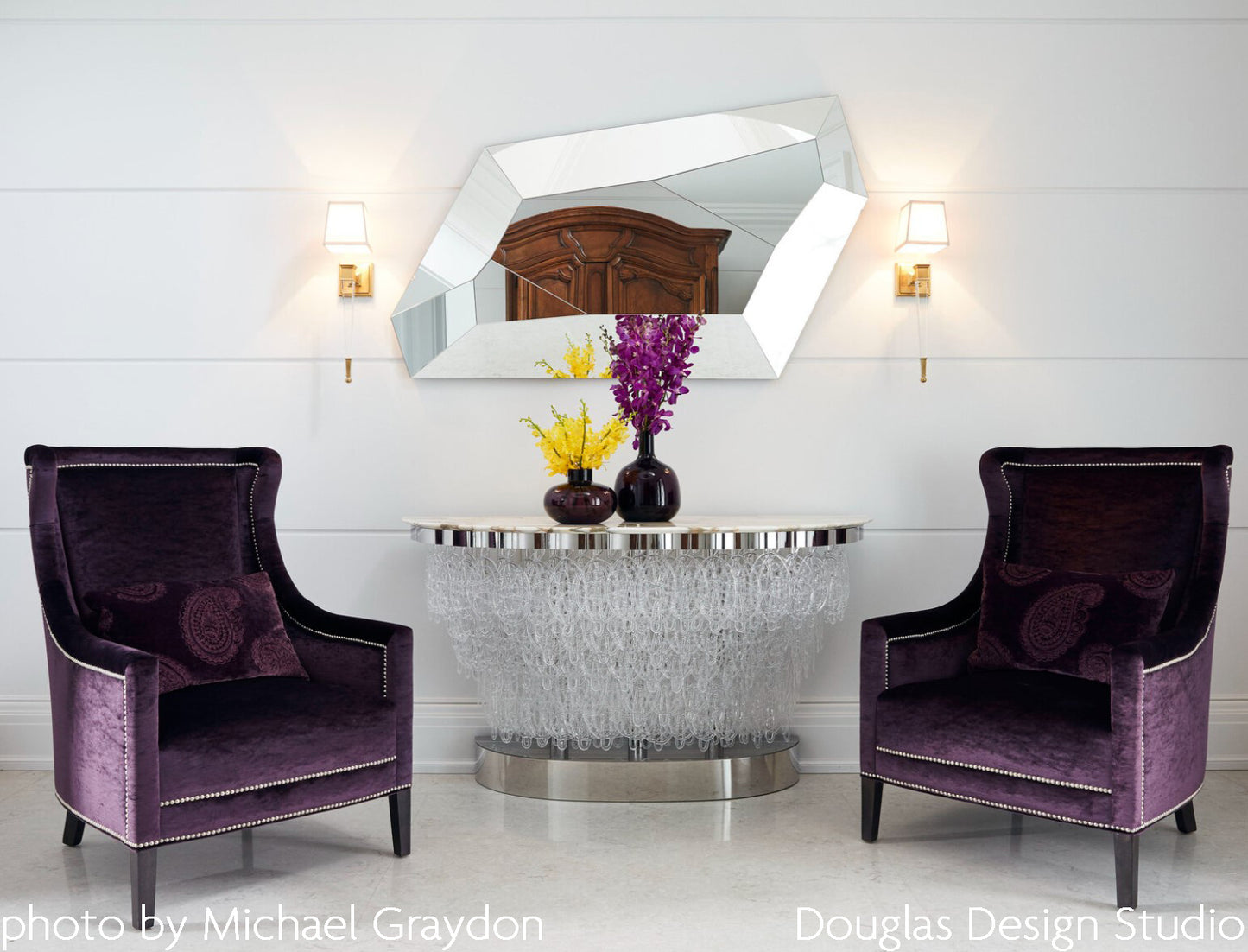 Crystal sconces with antique brass trim by mirror and purple chairs.