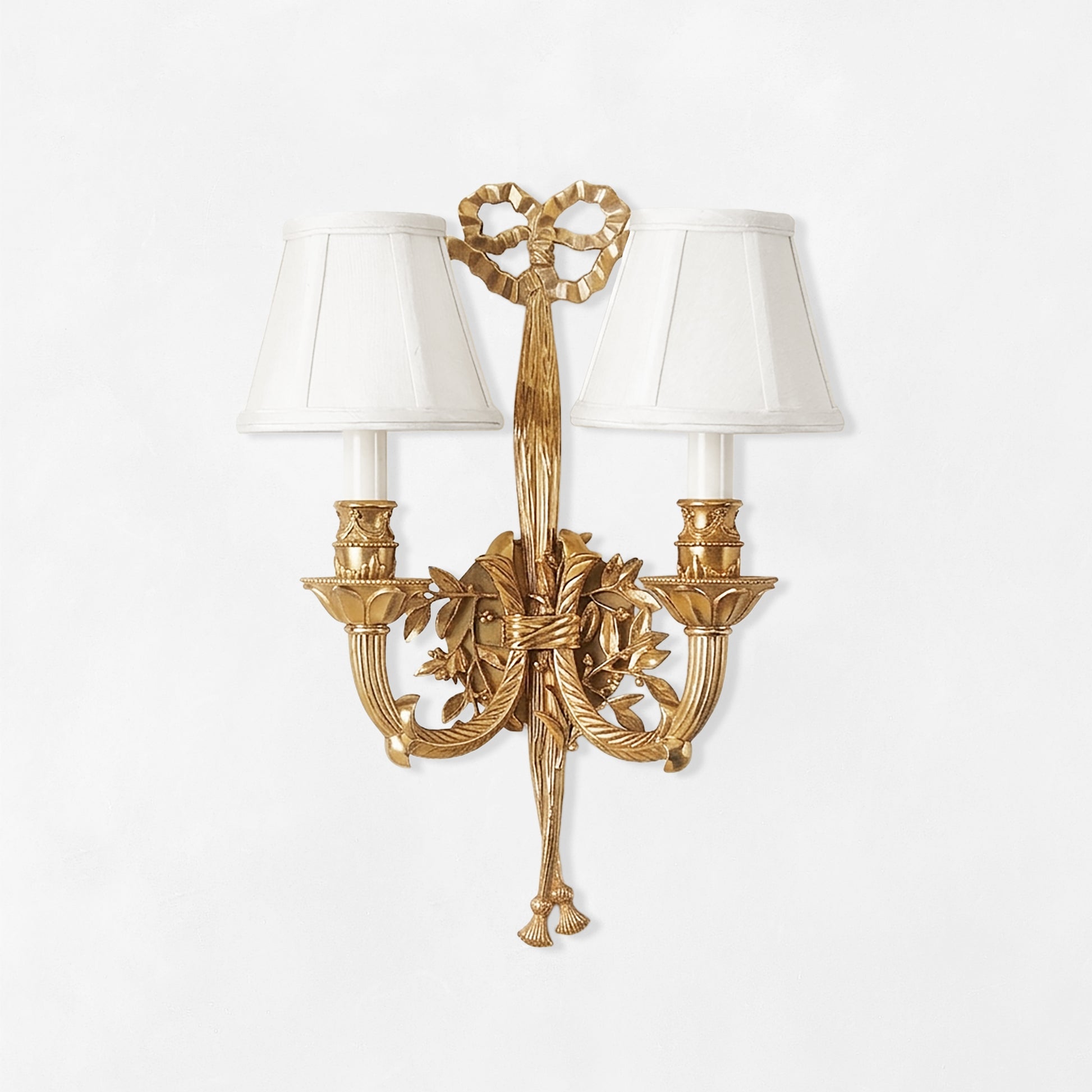 Ornate antique brass sconce with ribbon motif and white shades.