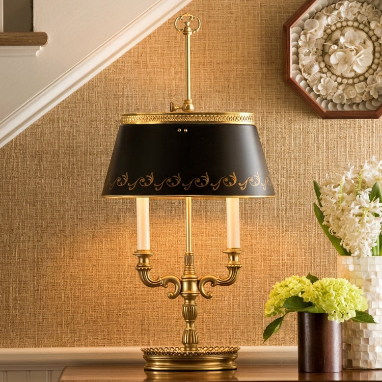 A brass bouillotte table lamp with a black shade styled with flowers in a foyer.
