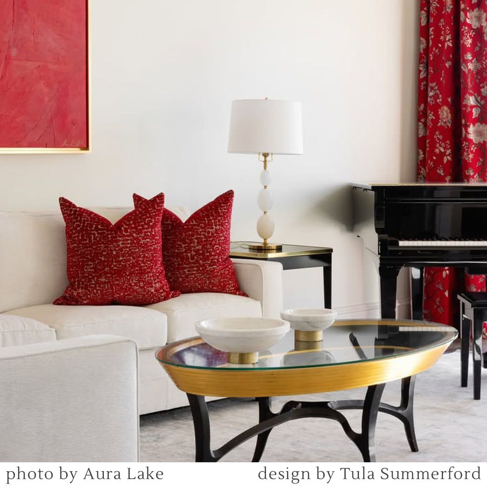 Living room with red pillows on a white sofa, glass coffee table, piano, and brass lamp.