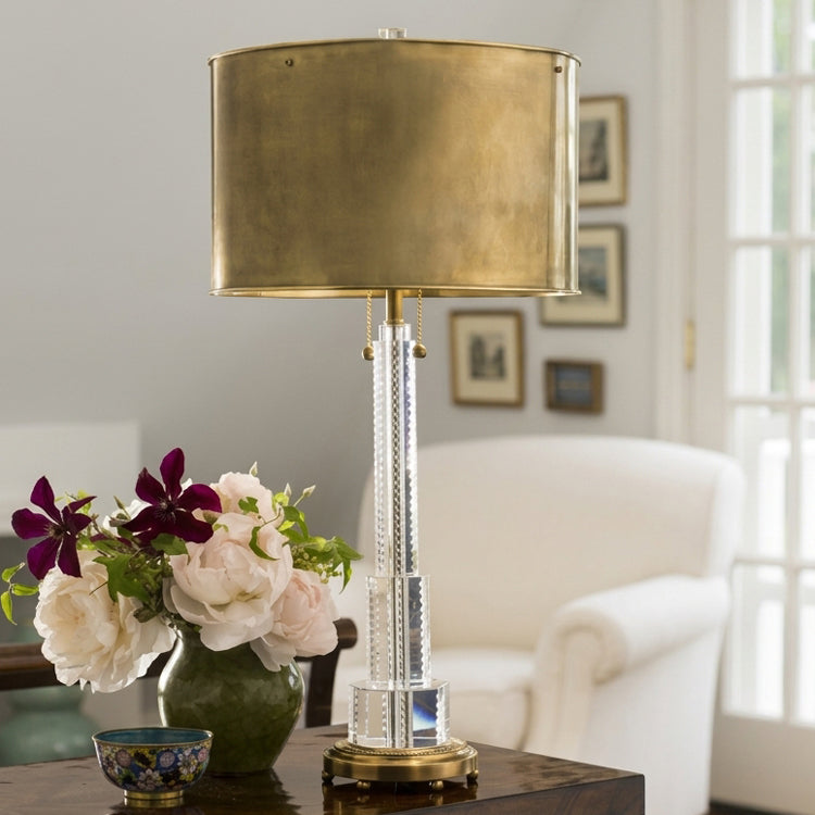 Luxurious crystal table lamp with antique brass lamp shade styled with flowers in an elegant living room.