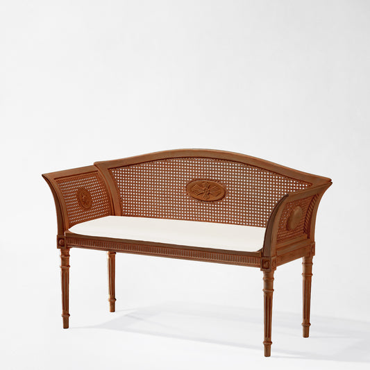 Brown cane bench with cream cushion.