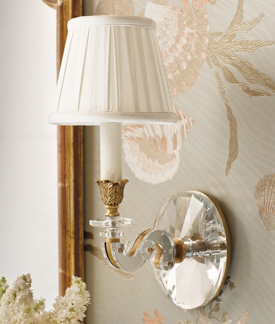 Crystal and brass sconce with pleated shade next to mirror.