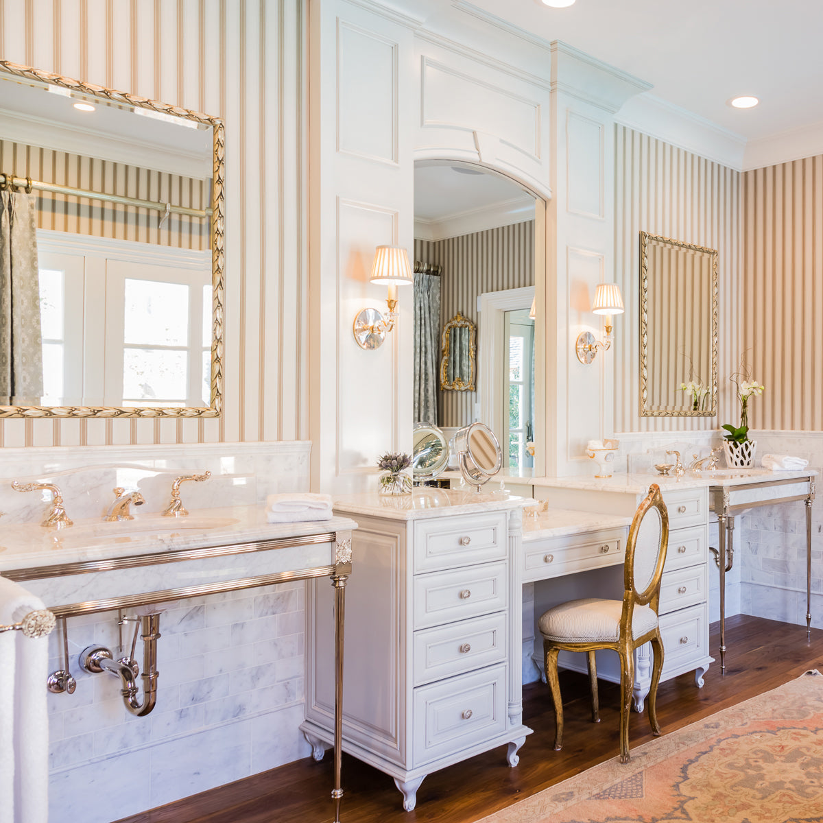 Crystal sconces with antique brass accents in bathroom with mirrors and chair.