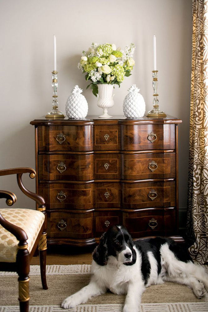 Crystal candlesticks on wooden chest of drawers with flowers.