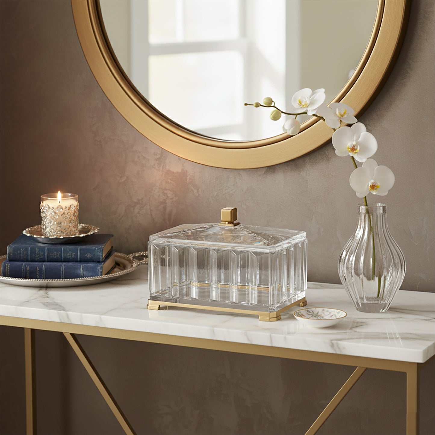 Decorative crystal box on marble console table with gold mirror and orchid in vase.