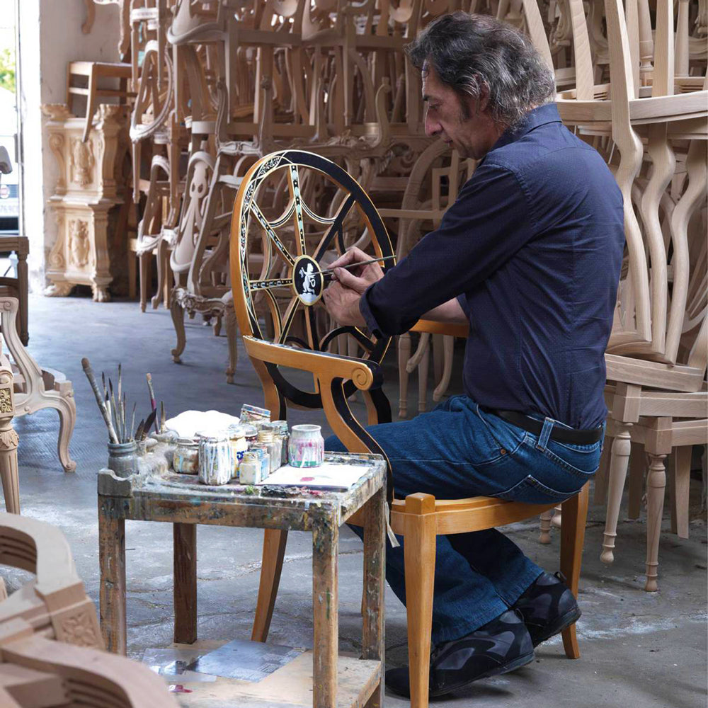 An Italian painter paints a luxurious wooden chair by hand in an Italian chair factory.