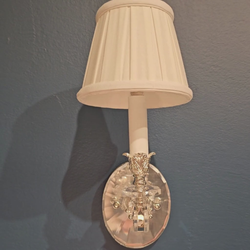 Crystal sconce with pleated white shade.