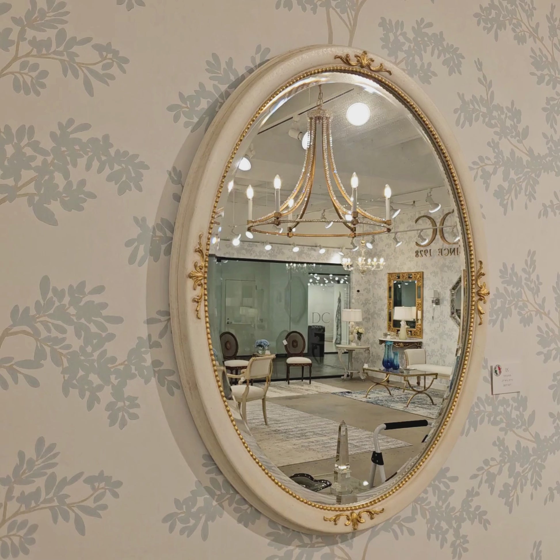 Oval white and gold Italian mirror on luxurious wallpaper.