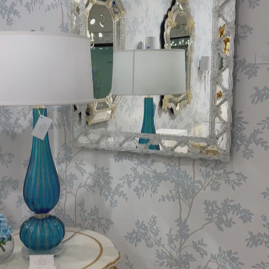 Murano glass mirror on luxurious wallpaper with blue Murano glass lamp.