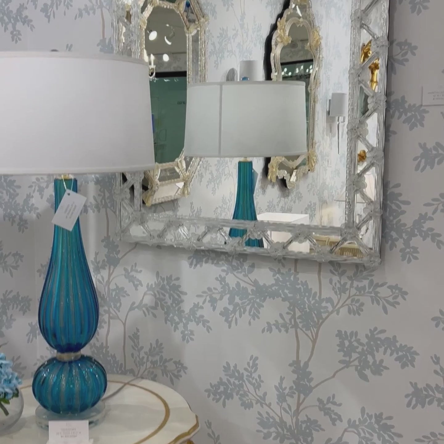 Murano glass mirror on luxurious wallpaper with blue Murano glass lamp.