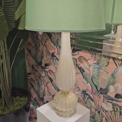 White Murano glass table lamp with light green lamp shade in front of pink designer wallpaper.