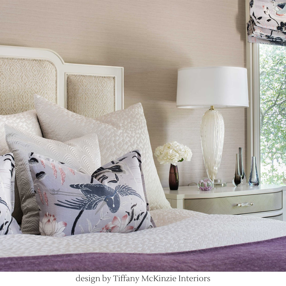 White Murano glass lamp next to bed with purple pillows.