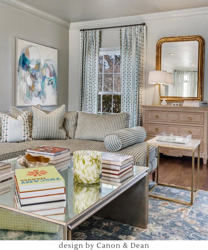 Upscale living room with a striped sofa, coffee table, gold mirror, and white table lamp.